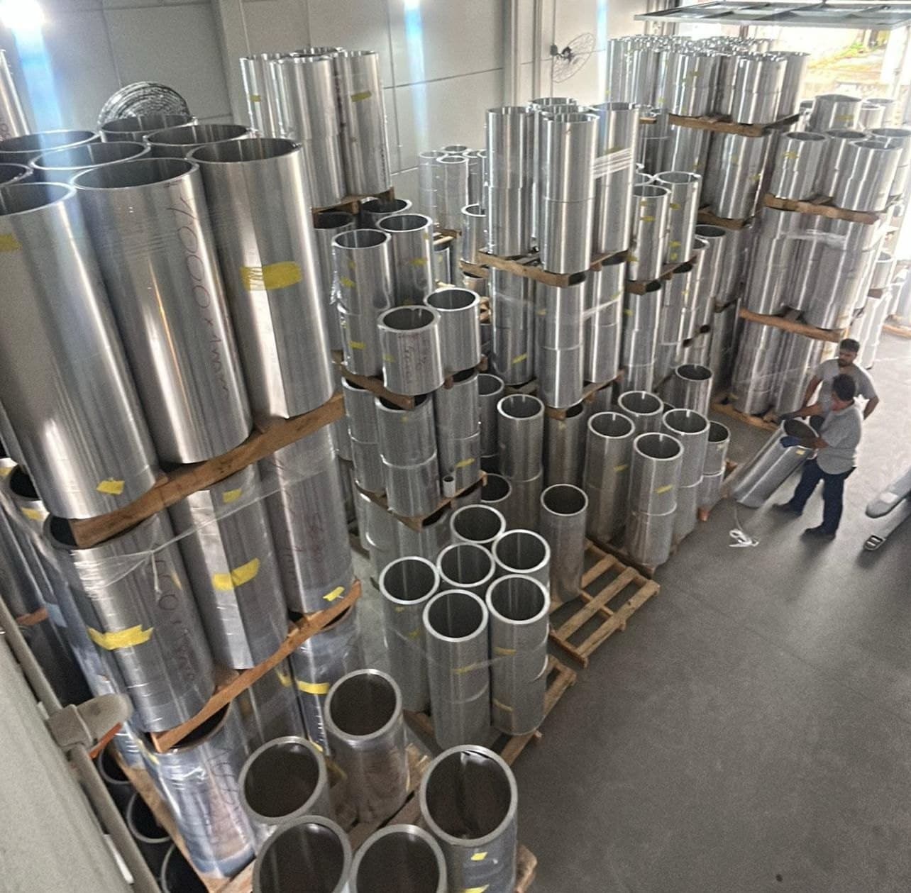 Estoque de bobinas de alumínio sobre paletes, com a equipe conferindo o material